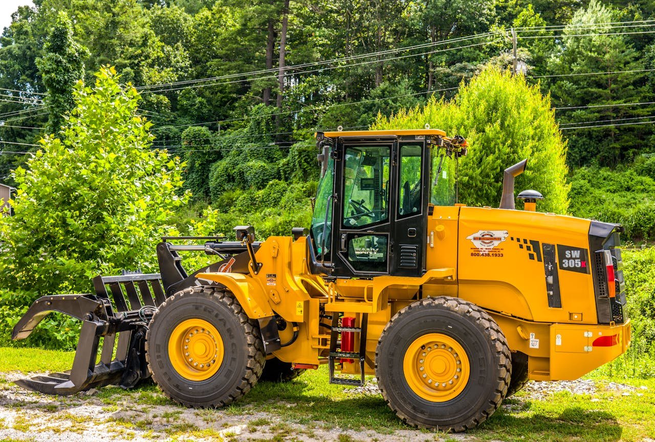 Services Yellow wheel loader parked outdoors in a forested area, showcasing machinery and natural contrast.